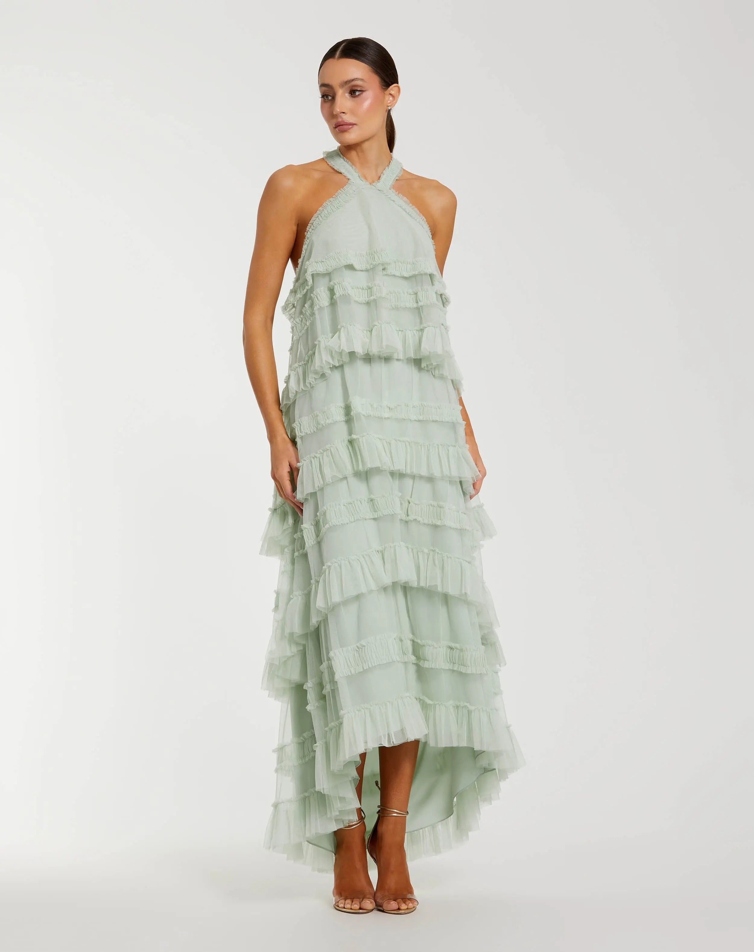 A woman wearing the Tea-Length Party Dress: Mac Duggal 8276 in Seamist, featuring a halter mesh ruffle design and high-low hemline, paired with strappy heels and standing against a plain white background.